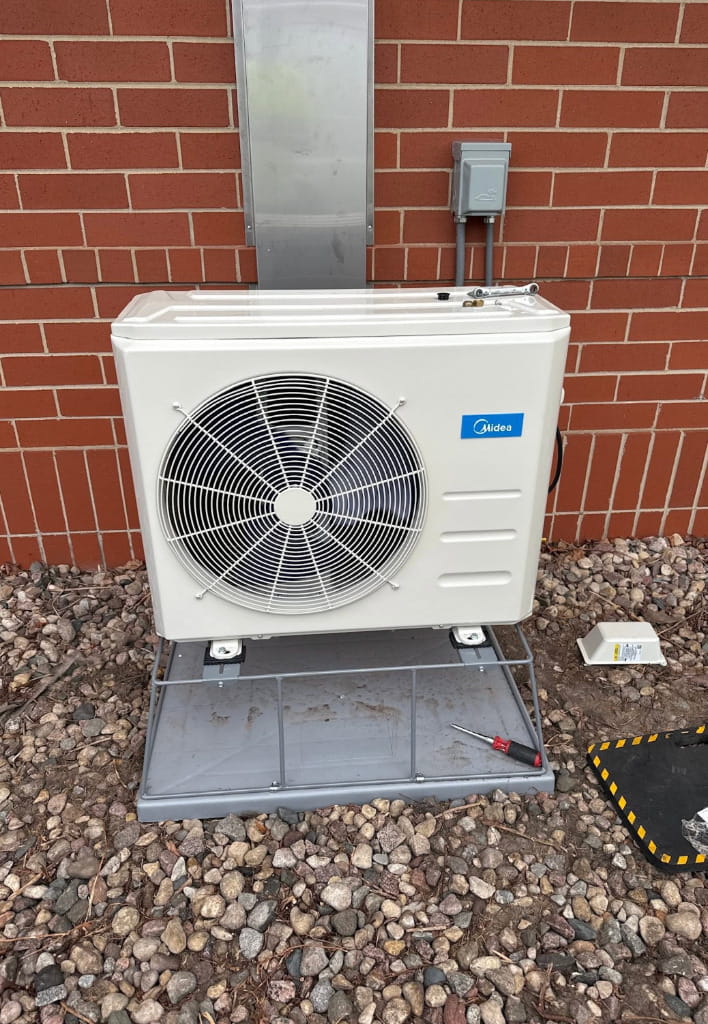 Outdoor ductless mini-split unit installed beside a brick building for efficient heating and cooling system performance.