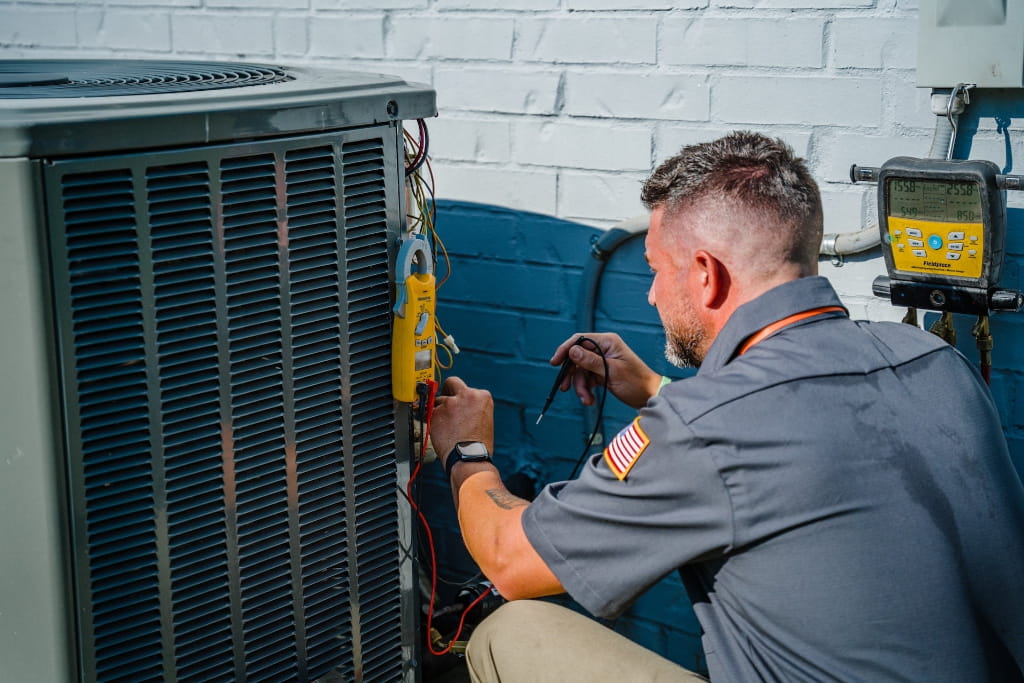 HVAC technician testing and servicing an outdoor air conditioning unit to improve cooling performance and system reliability.